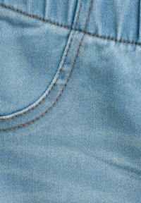 Svetlo modrá denímová látka s viditeľným švom vrecka a hnedým prešívaním, s jemnou textúrou a neformálnym dizajnom.