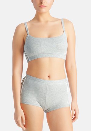 Frau trägt einen hellgrauen Sport-BH und passende hoch taillierte Shorts mit weißen Streifendetails.