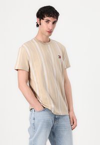 Beige striped T-shirt made of cotton, featuring white vertical stripes and a small logo accent on the left chest. Short sleeves, relaxed fit.