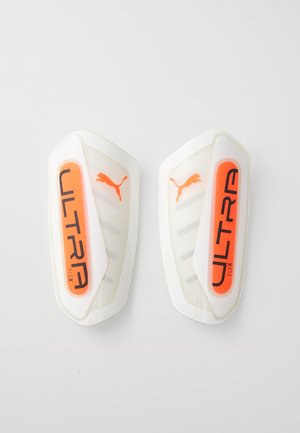 Parastinchi Puma Ultra Flex in bianco e arancione, con un design a guscio liscio, fasce elastiche e logo "ULTRA" sul davanti.