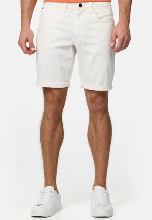 Witte spijkerbroekshorts met omgeslagen zomen, voorzien van zakken aan de voorkant en een zwarte knoop als detail. Draagt witte sneakers op een neutrale achtergrond.