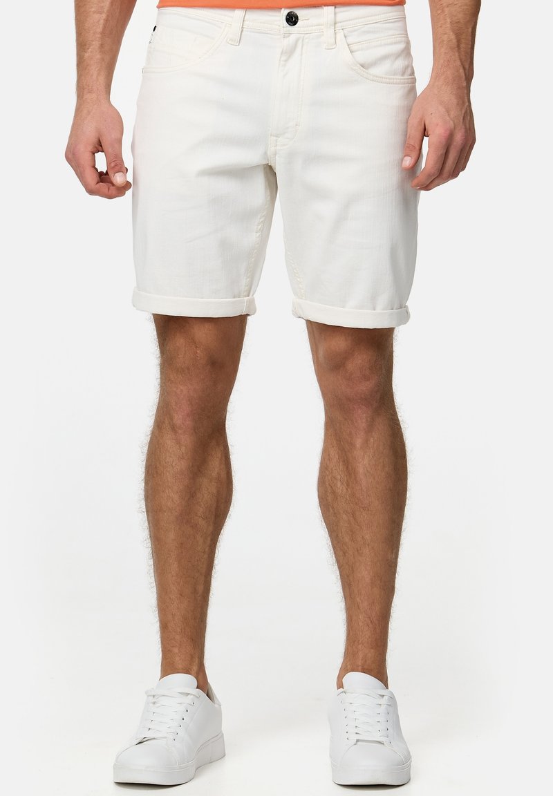 Shorts en denim blanc avec revers retroussés, dotés de poches avant et d'un détail de bouton noir. Portés avec des baskets blanches sur un fond neutre.