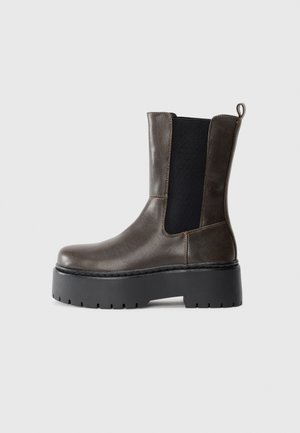 Botte en cuir marron mi-mollet avec panneau latéral élastique noir et semelle épaisse à crampons noire, vue de profil gauche sur fond blanc.