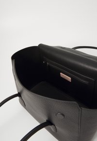 Sac fourre-tout en cuir noir avec une surface texturée, ouverture en haut, deux poignées, poche intérieure zippée et une petite étiquette de marque en rose.
