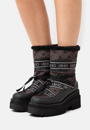 Kvinder sorte og brune vinterstøvler med tykke platformsåler, mønstret stof, kunstpelskant og båndsnørebånd omkring anklerne.