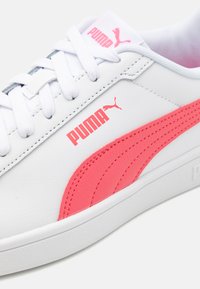 Bílé tenisky s růžovým logem Puma a bočním pruhem, s šněrovacím designem, hladkou koženou texturou a gumovou podrážkou.