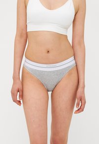 Sive bombažna bikini hlačka s pražnima belimi elastičnimi pasom, ki vsebuje logotip. Tkanina je gladka in oprijeta, s klasičnim rezom.