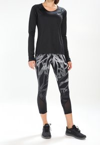 Zwart sportshirt met lange mouwen en ronde hals. Gecombineerd met zwart-grijze legging met patroon en mesh panelen. Zwarte sneakers maken de outfit af.