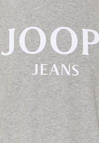 Grauer Stoff mit fettem weißen Text "JOOP" über kleinerem weißen Text "JEANS" bedruckt.