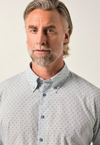 Světle šedá košile na knoflíky s jemným kruhovým vzorec, má klasický límec a světle modré knoflíky. Hladká textilie.