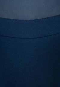 Tissu tricot bleu marine présentant une texture lisse et un léger éclat, avec un détail de couture courbe le long du bord supérieur.