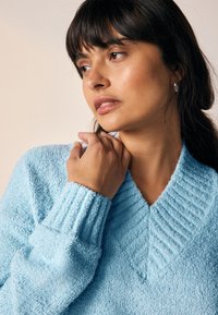 Taevassinine, tekstuuriga kampsun, millel on V-kaelus ja soonilised mansetid. Materjal tundub pehme ja karvane, lisades visuaalset huvi.