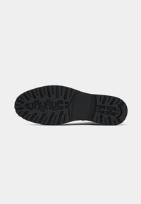 Suela de zapato de goma negra con un patrón de relieve texturizado, que incluye surcos y líneas elevadas para tracción y agarre.