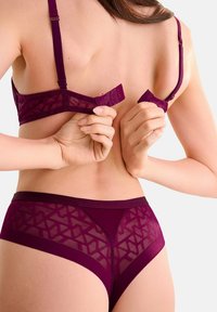 Bordeaux kanten beha met verstelbare bandjes en een haaksluiting, gecombineerd met een bijpassende slip met geometrische patronen en een gladde tailleband.