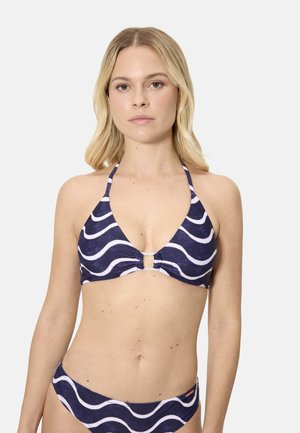 Mujer con bikini azul marino con patrones de olas blancas y un top halter con un detalle de anillo central, posando contra un fondo blanco liso.