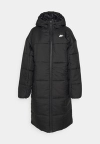 Melns pildīts garais mētelis ar kapuci, ar rāvējslēdzēju, elastīgām aprocēm un mazu balto Nike logo augšējā kreisajā pusē.