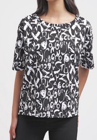 T-shirt nera a maniche corte con un motivo testuale astratto bianco, scollo tondo e vestibilità rilassata. Il tessuto appare liscio e leggero.