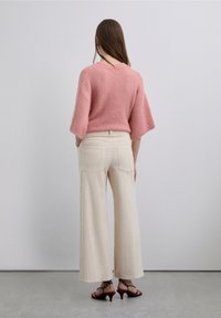 Pull rose clair texturé avec manches larges, associé à un pantalon large crème côtelé et des sandales à talons rouge foncé. Détail de boutons dans le dos.