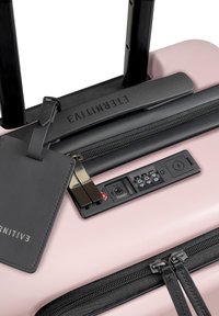 Hartschalen-Rosa-Koffer mit schwarzen Akzenten, einem TSA-Schloss, Reißverschlussfächern und einem schwarzen Gepäckanhänger am Griff befestigt.