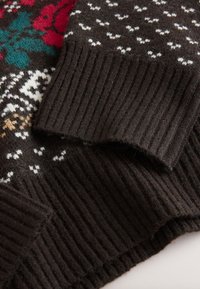 Pull marron en maille avec poignets côtelés, présentant des motifs floraux et géométriques multicolores en rouge, vert, blanc et beige.