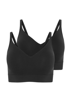 Schwarzes V-Ausschnitt-Bralette kombiniert mit weißen Shorts. Das Modell trägt ein leicht gestreiftes, knöpfbares Oberteil mit weicher Textur und lockerem Schnitt.