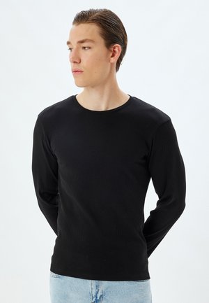 Czarna prążkowana koszula z długim rękawem i okrągłym dekoltem. Gładka tekstura, dopasowany krój i minimalistyczny styl, połączona z jasnoniebieskimi dżinsami.