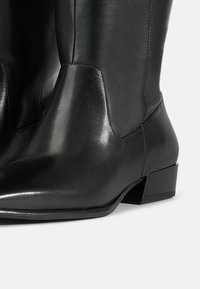 Zwarte leren enkelboot met een gladde textuur, ronde neus en lage blokhak. Beschikt over minimale stiksels en een slank ontwerp.