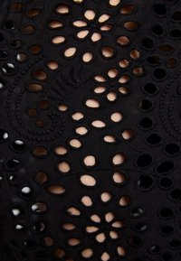 Tissu noir avec motif floral découpé brodé laissant apparaître des tons de peau clairs sous les trous.
