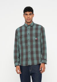 Skjorte i ternet flannel i brun og turkis, med krave der kan knappes ned, en lomme på brystet og et lille logo på brystet. Blød tekstur.