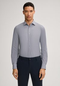 Herrenhemd mit Knöpfen, das ein kleines geometrisches Muster in Marineblau und Weiß aufweist. Es hat lange Ärmel, einen Kragen und eine taillierte Passform. Kombiniert mit dunklen Hosen.