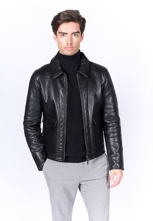 Chaqueta de cuero negra con cuello tipo solapa, bolsillos frontales y cierre de cremallera. Usada sobre un cuello de tortuga negro. Textura suave, diseño ajustado.