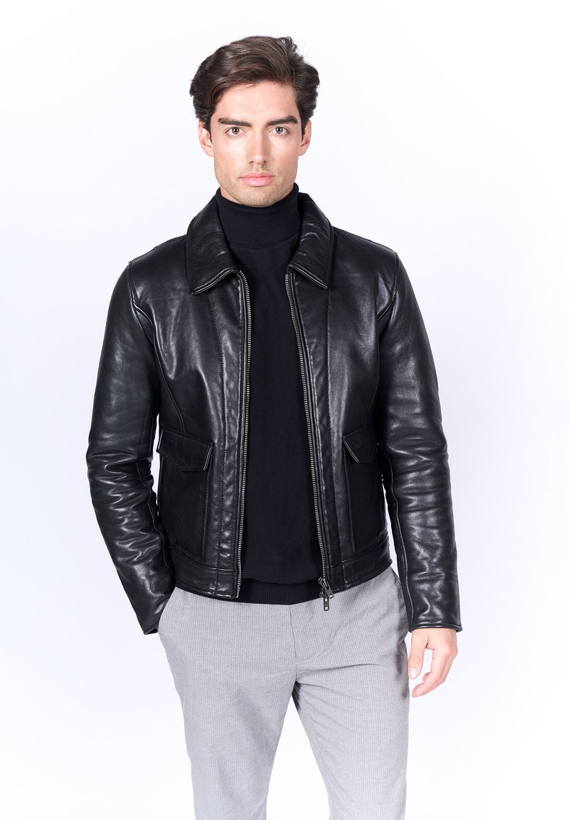 Chaqueta de cuero negra con cuello tipo solapa, bolsillos frontales y cierre de cremallera. Usada sobre un cuello de tortuga negro. Textura suave, diseño ajustado.
