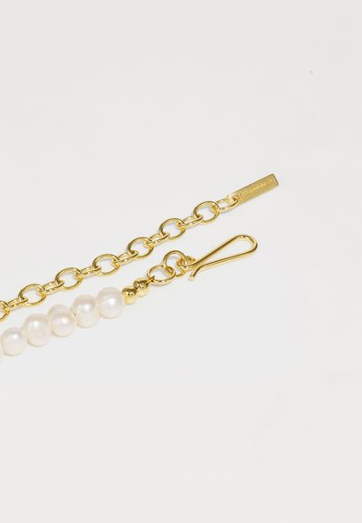 Guldhalsband med sektion av vita pärlor; har en spänne och varumärkesetikett, visar en blandning av släta och strukturerade element.