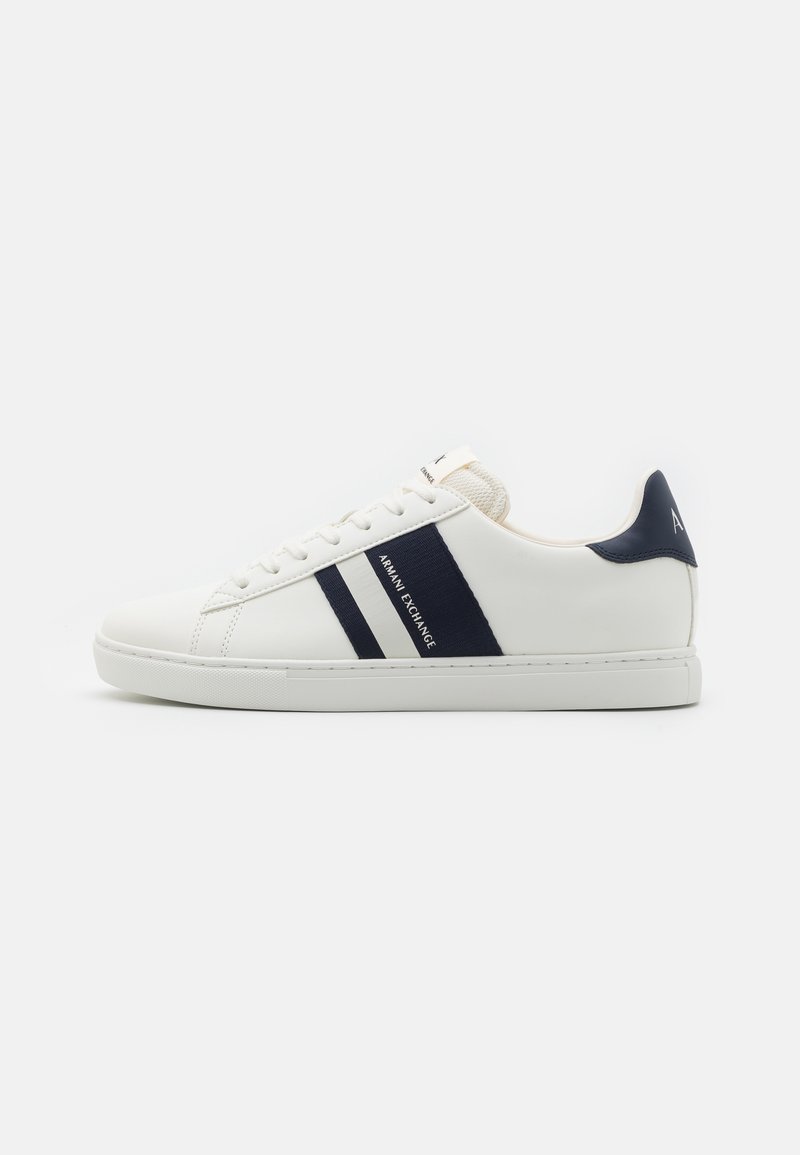 Sneaker in pelle bianca con accenti blu navy, caratterizzato da due strisce orizzontali e dettagli di marca, suola piatta e punta rotonda.