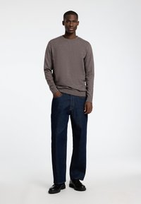 Grå langermet genser, teksturert stoff, kombinert med løstsittende mørkeblå jeans og svarte sko. Enkel, uformell antrekk.