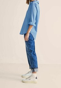 Blå och vit randig långärmad skjorta i kombination med denimjeans. Outfiten har uppvikta ärmar och vita sneakers med en mörk accent.