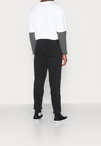 Svarta bomullssweatpants med en bakficka, sammansatta med en vit och svart randig långärmad tröja och svarta högskurna sneakers.