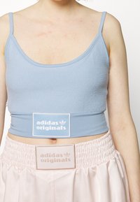 Svetle modrý bavlněný crop top s texturovaným povrchem, se bílou nášivkou loga. Spárován s růžovomodrou sukní s nařaseným pasem.