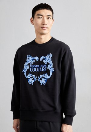 Sweatshirt noir en tissu mélangé de coton, avec un logo brodé bleu au design orné. Col rond et poignets et ourlet côtelés.