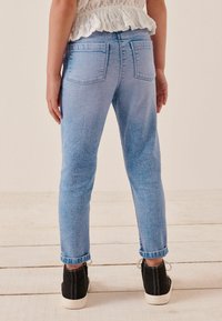 Ljust blå denimjeans med slim fit, uppvikta ärmslut och två bakfickor. Kombinerat med svarta skor med vit sula.