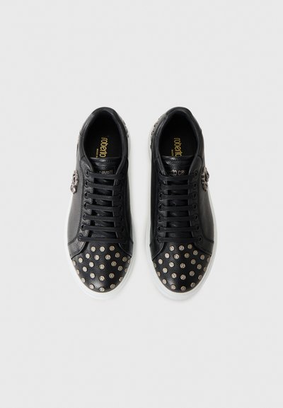 Sneaker in pelle nera con borchie argentate sulle punte, lacci neri e suole bianche, viste dall'alto su uno sfondo neutro.