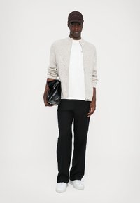 Ljusgrå stickad cardigan, vitt t-shirt, svarta byxor, vita sneakers och en svart clutchväska, med en brun keps. Enkel, modern design.