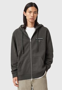 Dunkelgrauer Zip-Hoodie aus weichem Stoff, mit einer Kapuze mit Zugband, vorderen Taschen und einem Logo auf der linken Brustseite.