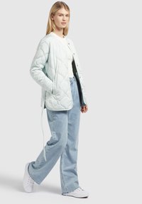 Lichtgroene gewatteerde jas met een ronde hals, drukknoopsluiting en zijzakken, gecombineerd met losse lichtblauwe jeans en witte sneakers.
