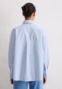 Striped blue and white long-sleeve shirt with a collar, featuring a relaxed fit and drop shoulder design. Textured cotton fabric.