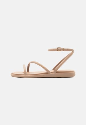 Sandale plate beige avec des brides fines, une boucle cheville et une boucle pour l'orteil, conçue pour un usage décontracté.
