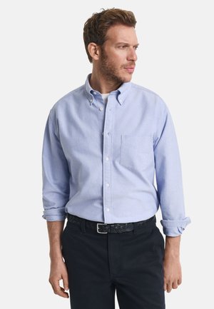 Lichtblauwe overhem shirt met lange mouwen, een borstzakje en opgerolde manchetten. Gepaard met een zwarte geweven riem en donkere broek.