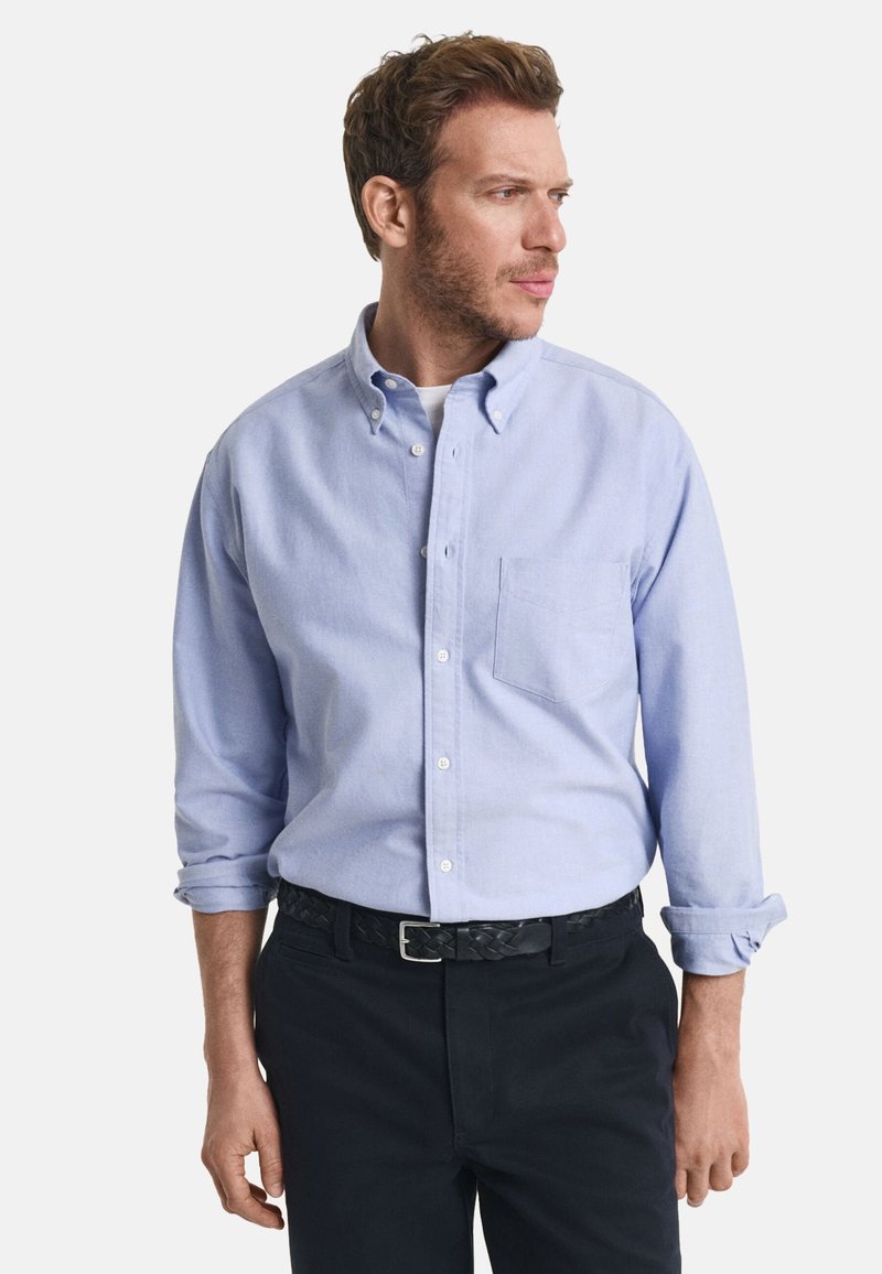 Helleblaue Hemd mit langen Ärmeln, einer Brusttasche und hochgerollten Ärmeln. Kombiniert mit einem schwarzen geflochtenen Gürtel und dunklen Hosen.