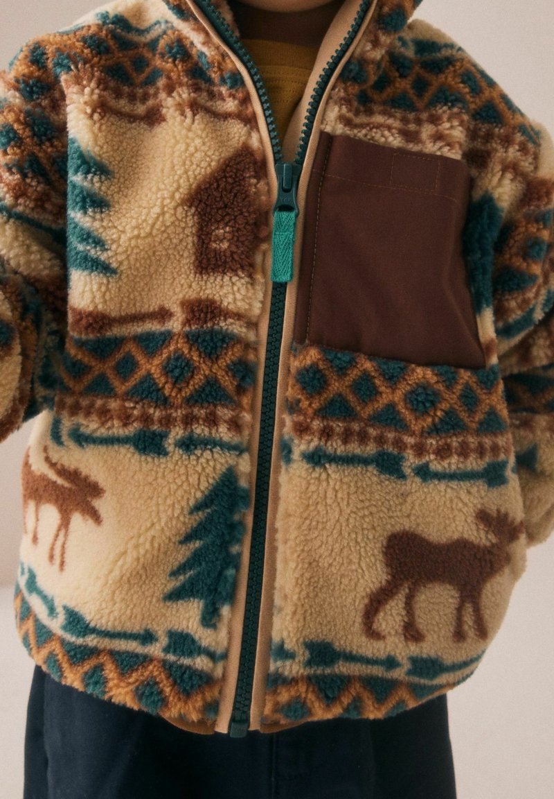 Enfant portant une veste polaire marron, bleu sarcelle et crème à motifs, avec une fermeture éclair frontale et une poche poitrine marron unie.