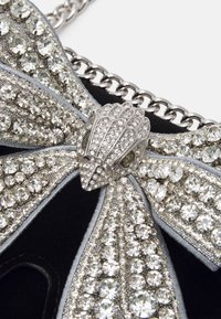 Czarna torebka na ramię z motywem kokardy, ozdobiona srebrnymi elementami i błyszczącymi cyrkoniami, z szarymi materiałowymi akcentami i łańcuszkiem.